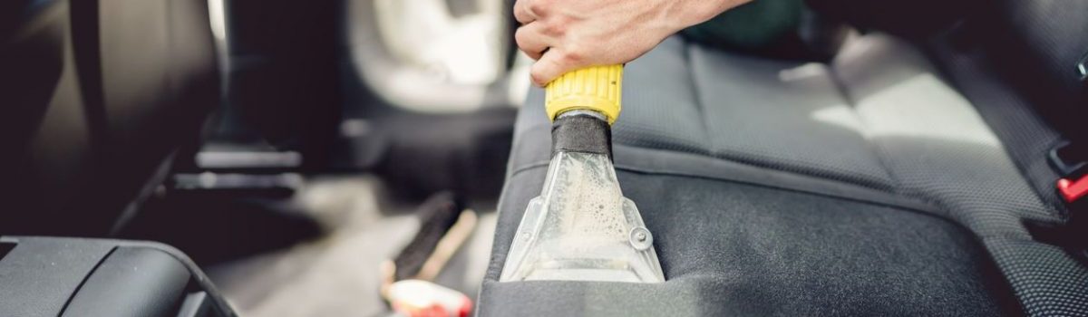 Car detailing and car care concept - Professional using steam vacuum for draining stains